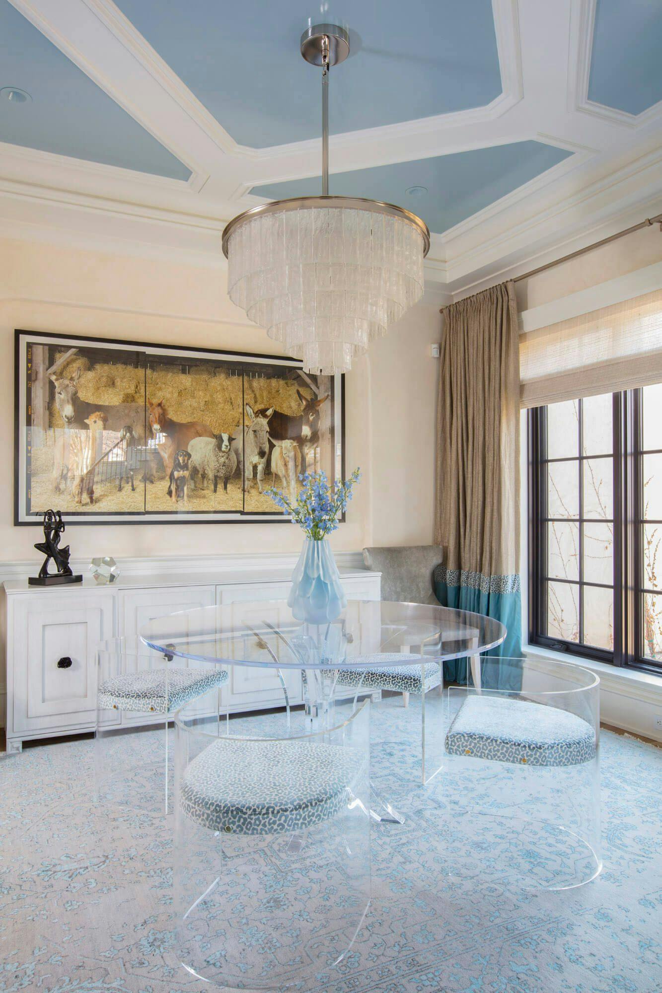 room with a clear table and clear chairs with a dangling chandelier and blue ceiling accents